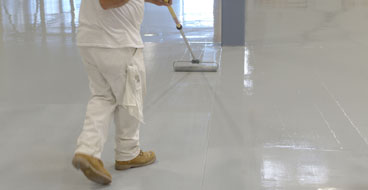 This image shows a man painting an industrial floor using a paint roller.