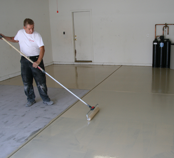 This image shows a man painting a floor with a roller brush.
